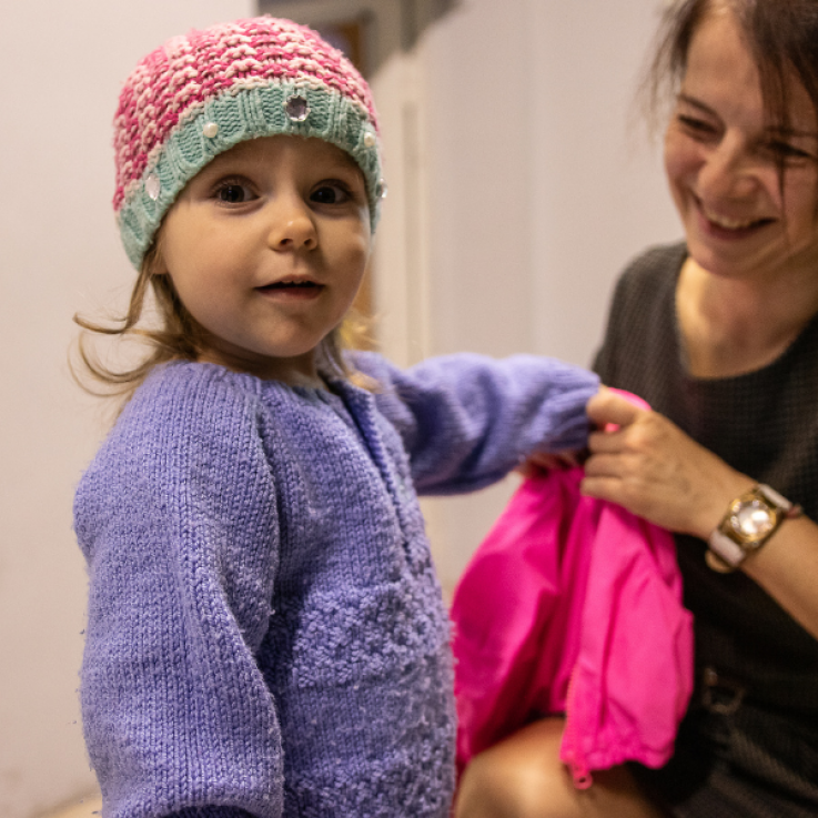 Bambina con maglione viola e cappellino di lana che indossa un giubbino invernale