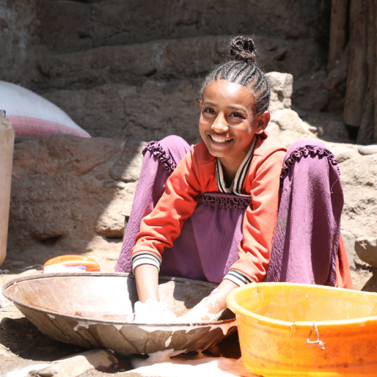 Bambina sorridente che lava dei vestiti all'aperto