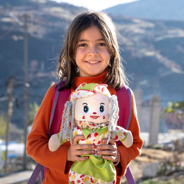 Bambina sorridente con in mano una bambola di pezza.