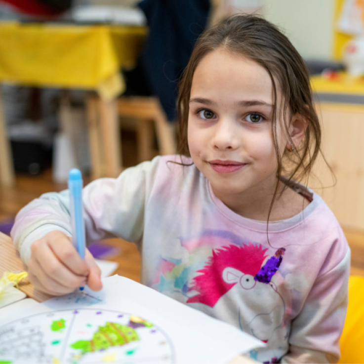 Bambina seduta su un banco di scuola con in mano una penna